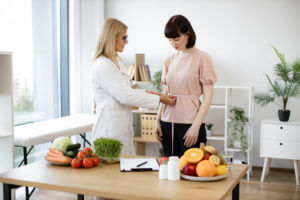 A female nutritionist measures the waist of her patient using a tape measure.