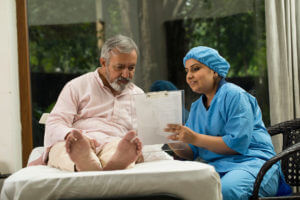 A female nurse is explaining the report to an elderly male patient in a hospital bed who has a chronic condition.